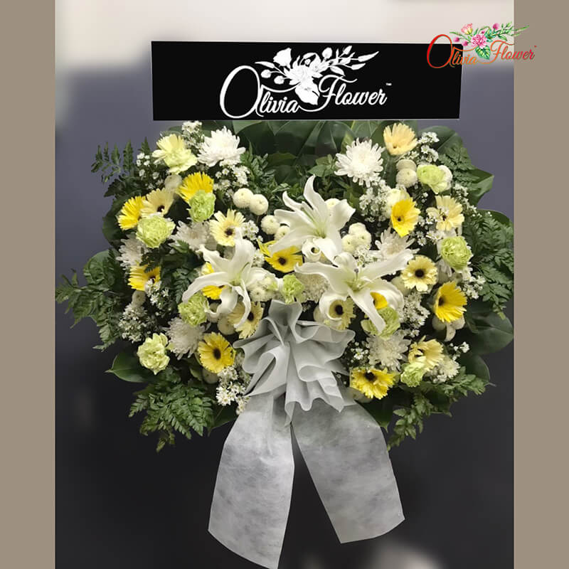 พวงหรีดดอกไม้สด ประกอบด้วย ลิลลี่ 3 ดอก ดอกเบญจมาศ เยอบีร่าสีขาว เยอบีร่าสีเหลือง คาร์เนชั่นสีเขียว และมัม