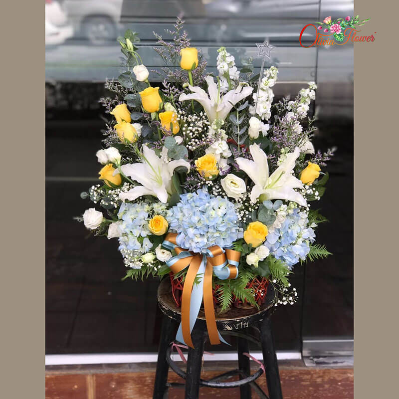 กระเช้าดอกไม้สด ประกอบด้วย กุหลาบสีเหลือง 10 ดอก ลิลลี่สีขาว สต็อคสีขาว ไฮเดรนเยียสีฟ้า ไลเซ็นทรัสสีขาว ยูคา แคสเปีย และยิปซี