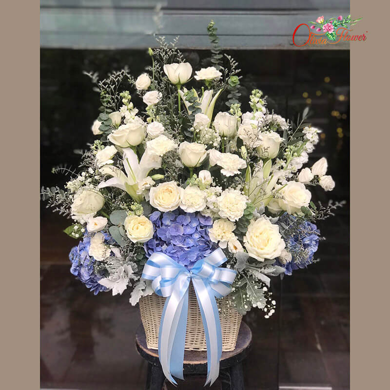 กระเช้าดอกไม้สด ประกอบด้วย กุหลาบสีขาว ลิลลี่สีขาว ไฮเดรนเยียสีฟ้า สต็อคสีขาว คาร์เนชั่นสีขาว ไลเซนทรัสสีขาว ใบยูคา และแคสเปีย